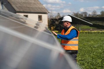 Male engineer in a hard hat and reflective vest inspects panels at solar power plant