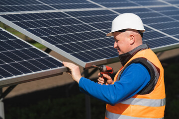 Obraz premium Solar power plant worker with electric wrench in his hands inspects panels
