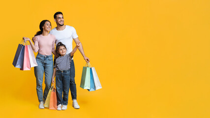 Shopping Offer. Arab Family Of Three Carrying Shopper Bags And Pointing Aside