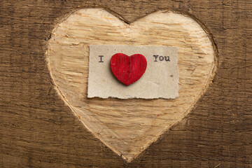I love you - tiny typed text note close up. Valentines Day greetings concept. Carved heart shape on wood as background for Valentines greeting card.