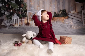 Fotobehang Kleinkind auf weißem Fell sitzend hält Nikolausmütze mit beiden Händen und blickt lachend nach oben © Ingeborg Zeh