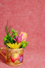 Arrangement of colorful, fresh cut flowers in a tiny teacup on a pink background, with copy space