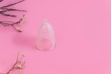 Silicone reusable menstrual cup on soft pink background with flowers and space for text