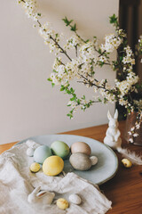 Obraz na płótnie Canvas Happy Easter! Easter eggs on plate with bunny figurines, linen napkin, cherry blossoms on rustic table. Natural dyed colorful eggs and spring flowers. Countryside still life