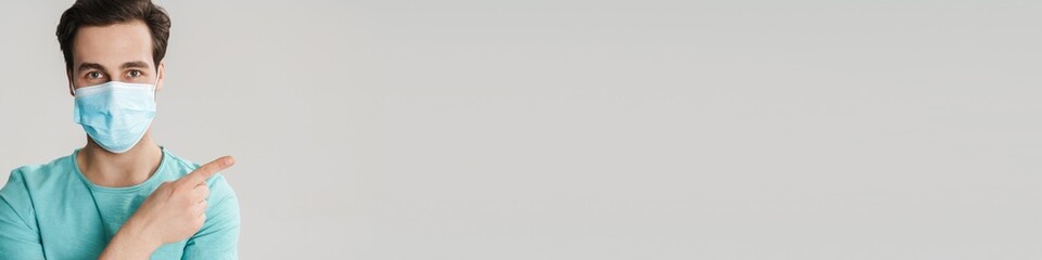 Caucasian handsome guy in protective mask pointing finger aside