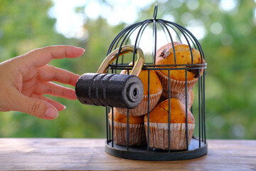 delicious biscuit cupcakes locked in an iron cage, rustic wooden table, male hand reaches for...