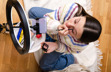 Top view of young teenage girl recording make-up tutorial video for social media on her smartphone. Gen Z influencers.