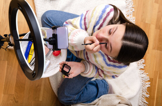 Top view of young teenage girl recording make-up tutorial video for social media on her smartphone. Gen Z influencers.