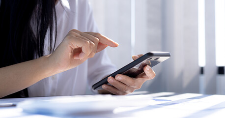 Business woman holding a smartphone and pointing at the screen, she is typing a chat message with her partner using a smartphone messenger. Concept of using technology in communication.