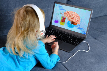 small child, a blonde girl 2 years old lies on the sofa in front of a laptop, dna molecules sign,...