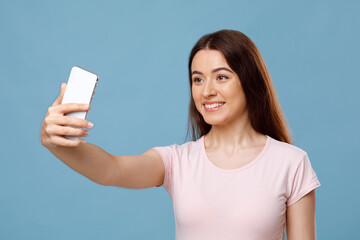 Naklejka premium Attractive young lady taking selfie on blue studio background
