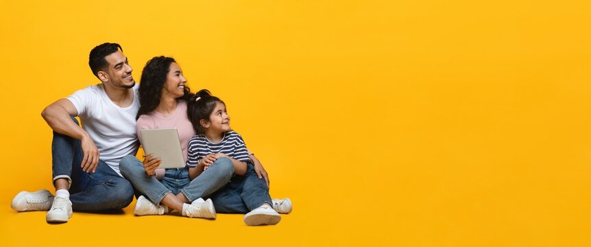 Happy Young Arab Family Of Three Holding Digital Tablet And Looking Aside