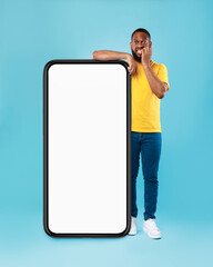 Black guy leaning on giant smartphone with blank screen, biting nails in panic, afraid to miss web store sale, mockup