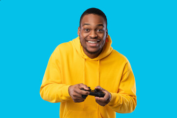 Cheerful Black Guy Playing Videogame Holding Game Controller, Blue Background