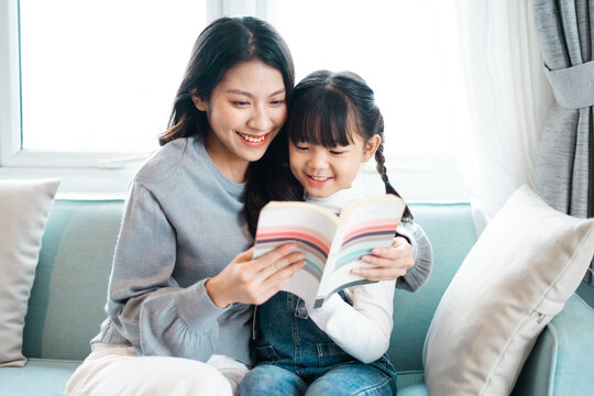 image of mother and daughter sitting on the sofa reading a book