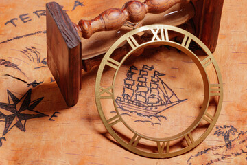 An hourglass and clock face lying on the order of antique nautical chart depicting sailing ships.