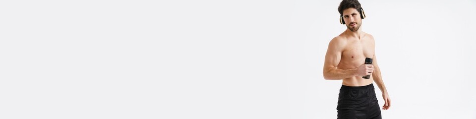 Fototapeta premium Shirtless athletic sportsman in headphones posing with water bottle