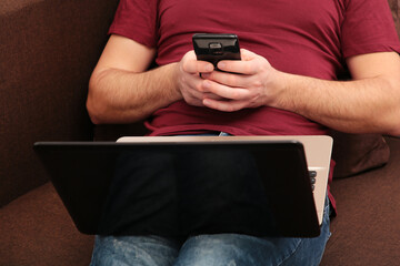 Young man working at home using laptop and smartphone