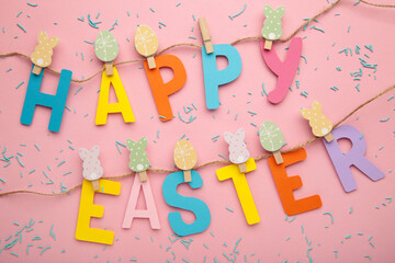 Inscription Happy Easter on pink background, a rope with clothespins. The concept of postcards for the Easter holiday.