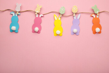 Easter rabbits handmade from colored paper on a rope with clothespins easy crafts for children on a pink background.