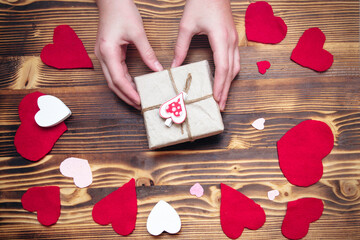 Hands holding a box in kraft paper with a heart-shaped decor on a background decorated for Valentine's Day. Gift for a loved one concept. Soft focus