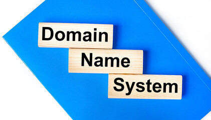 There is a blue notebook on a light gray background. Above are three wooden blocks with the words DNS Domain Name System