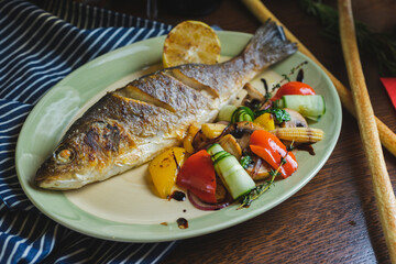 Grilled white fish on a dish on a table in a restaurant with a glass of white wine.