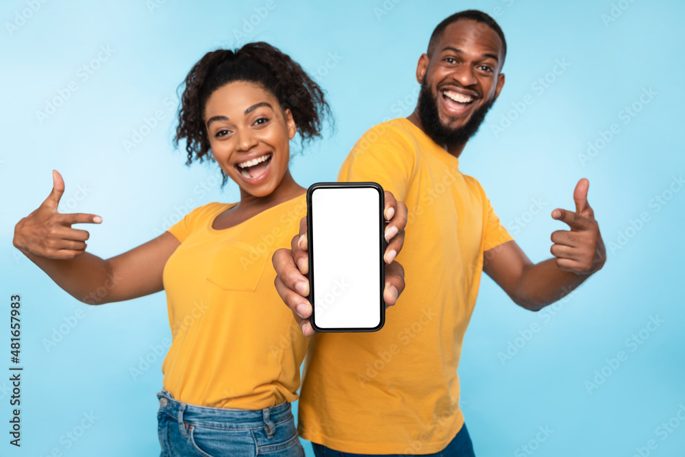 Poster excited afro couple pointing at cellphone with blank screen, recommending new app on blue background