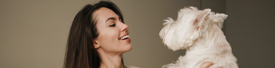 Happy young woman playing with her dog in bedroom