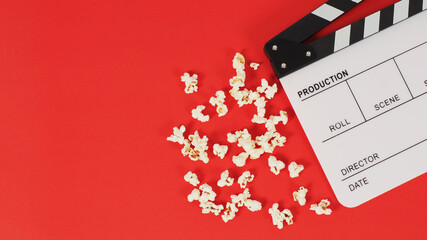 Clapper board or movie slate and popcorn on a red background.