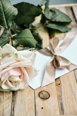 Marriage proposal. Rose and envelope with a bow on wooden background. Desired gift. Delicate still life. Woman's day morning