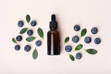 Flat lay composition with serum glass dropper bottle and many blueberries and green leaves on light...