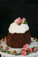 Easter cake with white icing decorated with flowers on a white stand on a black background.