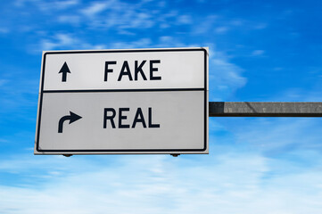 Road sign with words fake and real. White two street signs with arrow on metal pole on blue sky...