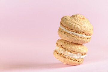 Two beige macaroons in a stack close-up on a pale pink background with copy space