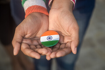 A young girl holding a metal badge with Indian flag colors in her palm. A conceptual photo depicting a love and respect for mother India.