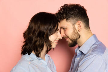 Closeup young and happy man and woman look at each other isolated on pink trendy color background. Human emotions, youth, love and lifestyle concept