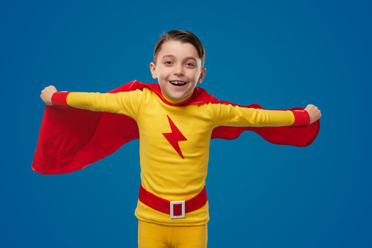 Cheerful boy in superhero cape flying in studio