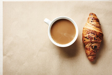 Cup of coffee with cream and chocolate croissant.