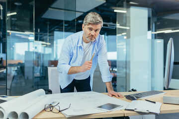 Experienced architect, working at the office desk on the drawing, makes final edits before handing over the object, a man in a modern office