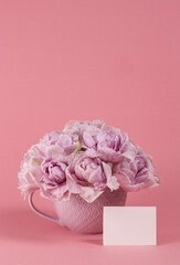 Violet tulips in vase with blank greeting card. Place for text. Mock up. Tulips in vase on pink background