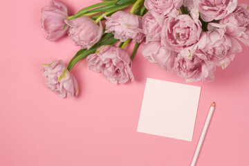 Tulips with blank greeting card on pink background. Place for text. Mock up greeting concept.