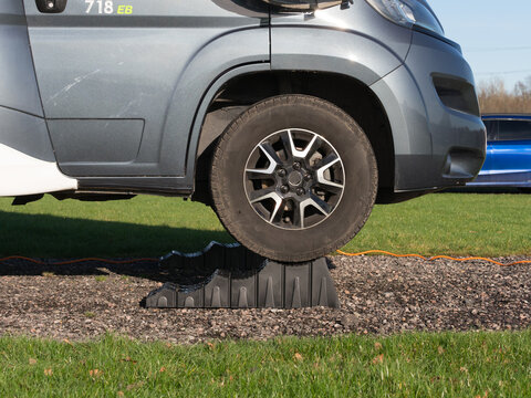 The front wheel of a motorhome recreational vehicle has been raised up by driving vehicle up a black levelling block.Viewed from side.Level.RV.