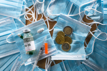 Close up photo of medical masks with coins and vial of coronavirus vaccine with sterile syringe on...