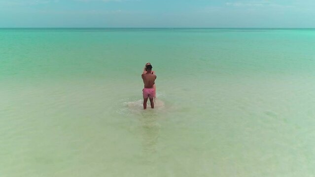 Happy honeymoon couple holding hands and spinning in shallow blue water