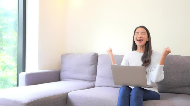 A young woman working on her laptop reacts in triumph as she completes her task. Title space