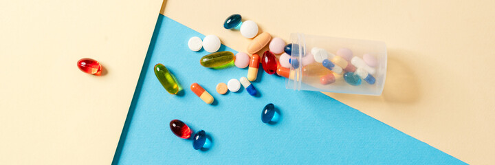 Overhead view of a scattered multicolored pills in a transparent jar lying on a colored background