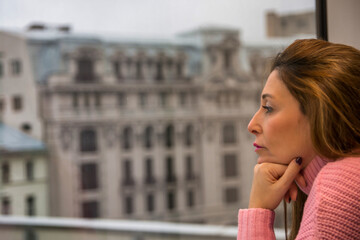Fototapeta na wymiar Woman Next To A Window And Looking Away. She Is Contemplating The Panorama Outside, Looking Outside Through A Window