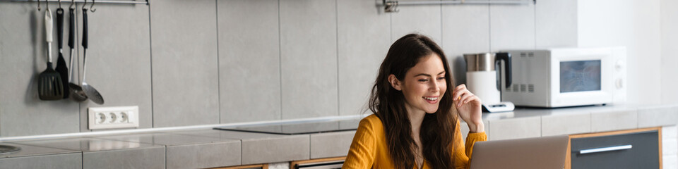 Brunette young woman sitting at the kitchen table with laptop