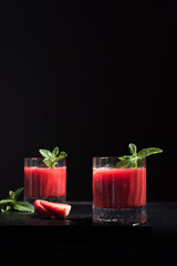 Dos vasos de refrescante jugo de fresa triturado decorado con una rama de menta y fresas cortadas sobre un fondo negro